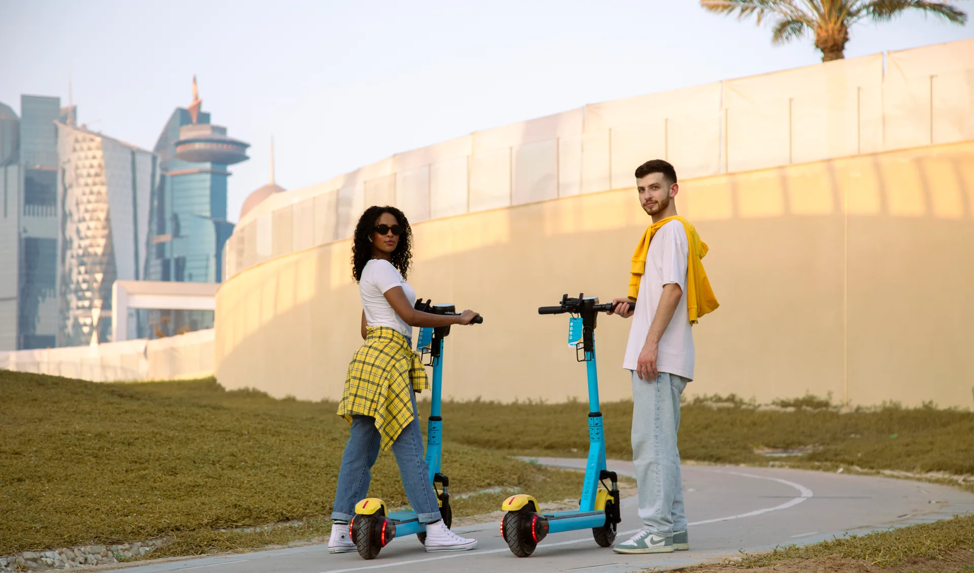 Two friends beside their Loop scooters on a sunlit city path in Qatar