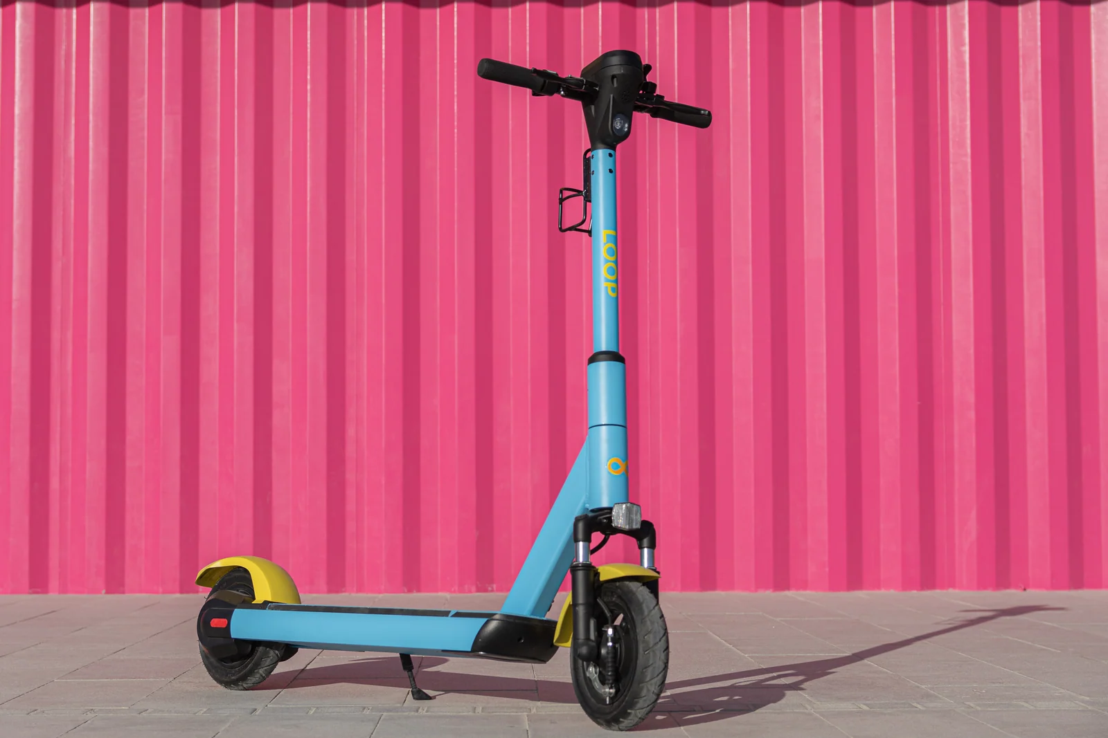 A Loop scooter resting on its stand against a pink wall, with the entire scooter visible